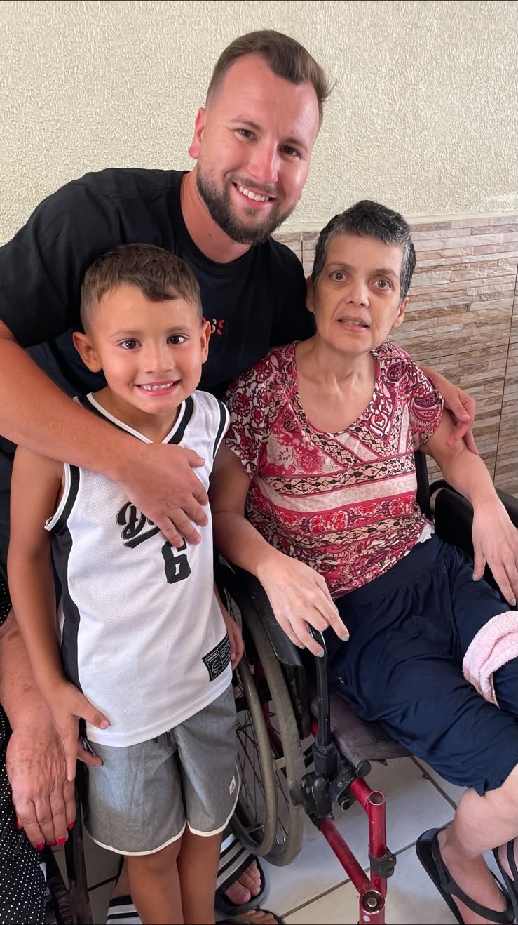 Renan e o filho abraçados a uma moradora em cadeira de rodas
